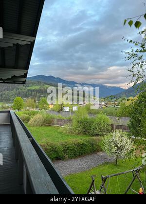 Ein ruhiger Blick vom Balkon auf ein üppiges grünes Tal, umgeben von fernen schneebedeckten Bergen unter einem bewölkten Himmel in Österreich. Perfekt für r Stockfoto