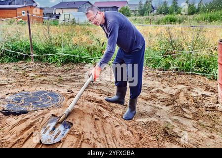 Arbeiter verdichten Sand um die Kanalabdeckung des Entwässerungsbrunnen mit einer Schaufel. Stockfoto