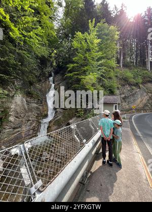 Eine Familie genießt einen ruhigen Moment an einem Wasserfall in einem lebendigen Wald. Die Sonnenstrahlen blicken durch die Bäume und tragen zur ruhigen Atmosphäre bei Stockfoto