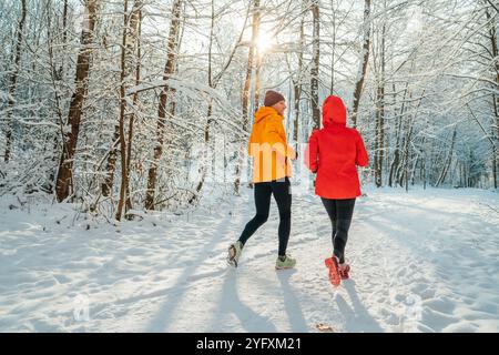 Lächelnde Läuferinnen und Läufer mittleren Alters trugen helle winddichte Jacken und liefen während der sonnigen Eiszeit im malerischen, schneebedeckten Wald Stockfoto