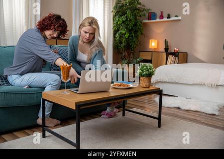 Freunde, die an einem Laptop in einem gemütlichen Wohnzimmer zusammenarbeiten und sich gegenseitig Gesellschaft genießen Stockfoto