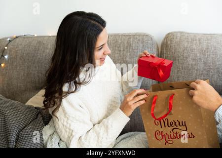 Schöne brünette Frau, die Weihnachtsgeschenke von ihrem Partner erhält. Das Konzept der weihnachtsfeiertage zu Hause mit der Familie Stockfoto