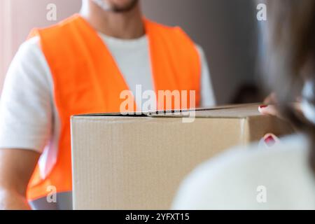 Der Liefermann gibt dem Kunden zu Hause ein Papppaket. Großaufnahme der Hände und der Kiste. Nicht erkennbare Personen. Stockfoto