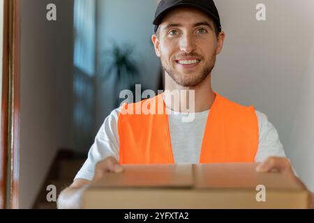 Nahaufnahme eines attraktiven Liefermannes mit Pappkarton in den Händen. Lieferung eines Pakets nach Hause beim Kunden Stockfoto