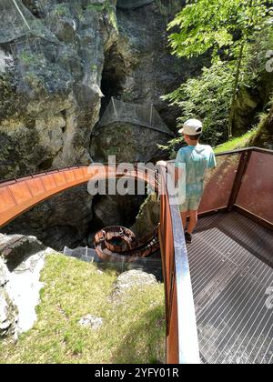 Eine junge Person steht auf einem Metallsteg mit Blick auf einen Spiralweg in einer üppigen Schlucht in der Liechtensteinklamm, Österreich. Die Szene strahlt Abenteuer aus Stockfoto