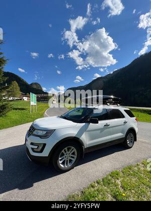 Ein weißer Geländewagen, der auf einer gewundenen Bergstraße mit üppigem Grün und einem hellblauen Himmel mit Wolken geparkt ist, hält eine perfekte Outdoor-Reiseszene fest Stockfoto