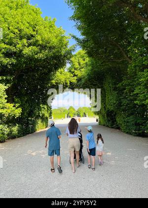 Eine Familie genießt einen gemütlichen Spaziergang durch einen lebendigen grünen Park unter klarem blauen Himmel im Schloss Schönbrunn, Österreich. Die Szene fängt das Wesen von ein Stockfoto