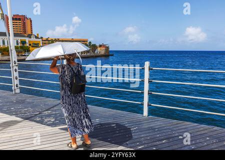 Frau mit UV-Schirm auf der Queen Emma Pontoon Bridge über St. Anna Bay in Willemstad, Curacao. Willemstad. Curacao. Stockfoto