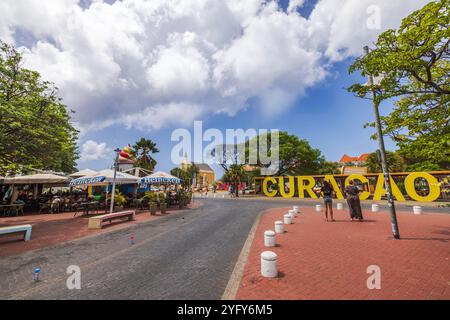 Café mit Heineken Schild in der Nähe großer gelber Curacao Buchstaben auf einem offenen Platz unter bewölktem Himmel. Willemstad. Curacao. Stockfoto