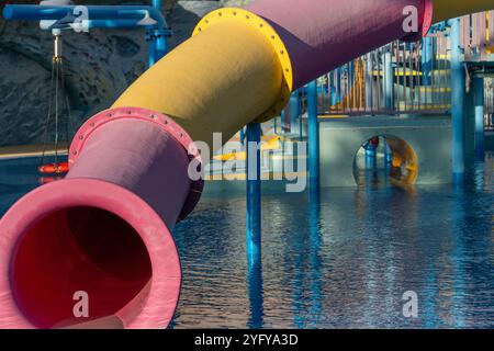 Waterpark Slide Pool Fun - Nahaufnahme einer rosa und gelben Wasserrutsche in einem Wasserpark. Die Rutsche befindet sich über einem blauen Pool. Stockfoto