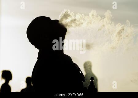 Salvador, Bahia, Brasilien - 21. Dezember 2019: Silhouetted man wird in Salva an einem sonnigen Tag während Sonnenuntergang im Freien gesehen, wie er eine E-Zigarette raucht Stockfoto