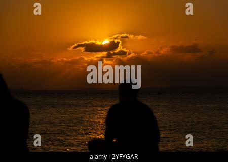 Salvador, Bahia, Brasilien - 22. Oktober 2024: Unbekannte Menschen in Silhouette genießen den dramatischen Sonnenuntergang in Porto da Barra. Salvador, Bahia. Stockfoto