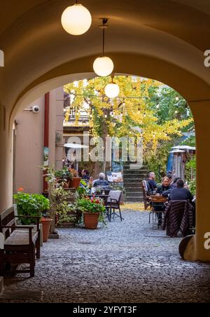 Szene in der Prager Altstadt, Tschechien, im Herbst, von einem geschlossenen Durchgang mit Bogendach, der zu einem charaktervollen Café in einem Innenhof zwischen Gebäuden führt. Stockfoto