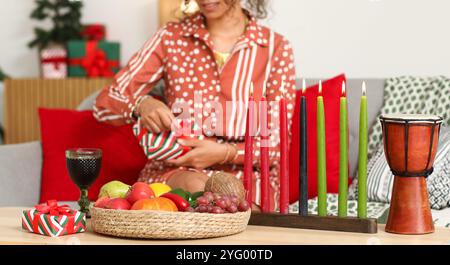 Brennende Kerzen mit Essen auf dem Tisch und Frau, die zu Hause ein Geschenk auspackt Stockfoto