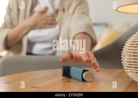 Frau, die nach Asthma-Inhalator greift, an Holztisch drinnen, Nahaufnahme Stockfoto