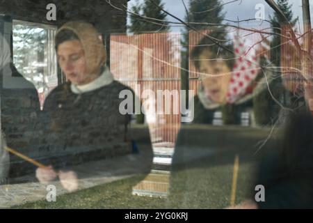 Iryna B. und Natalia (von links nach rechts), drei ukrainische Flüchtlinge, beten für ihre in der Ukraine zurückgelassenen Angehörigen, für die Seelen gefallener russischer Soldaten und sogar für Putin im orthodoxen Kloster Putna in Rumänien, wo sie sich aufhalten. Nach der Invasion Russlands in die Ukraine im Jahr 2022 fanden zwei ukrainische Familien Zuflucht im orthodoxen Kloster Putna in Rumänien: Iryna B., eine ehemalige Englischlehrerin, ihre Schwiegermutter Natalia, ihre beste Freundin namens Iryna und ihre fünf Kinder. 24 km von der ukrainischen Grenze entfernt, füllen sie ihre Tage mit Online-Bildung, Anrufen von Verwandten, Spaziergängen und Stockfoto