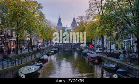 Amsterdam 23. Oktober 2024, goldene Blätter schweben sanft auf dem Wasser, während die Dämmerung über Amsterdams berühmten Kanäle herabsteigt. Charmante Boote und Jahrhunderte alte Stockfoto