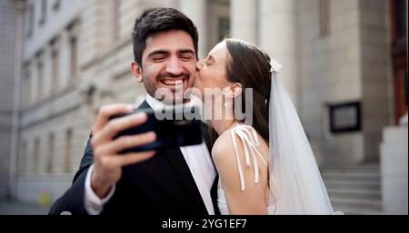 Paare, Selfie und Küsse mit Hochzeit in der Stadt, Liebe und glücklich für Engagement, Erinnerung und Post im Internet. Menschen, Mann und Frau mit Ehe, Ereignis und Stockfoto