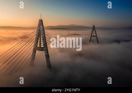 Budapest, Ungarn - Blick aus der Vogelperspektive auf die wunderschöne Megyeri-Hängebrücke über die Donau, die an einem Herbstnachmittag in starkem Nebel bedeckt ist Stockfoto