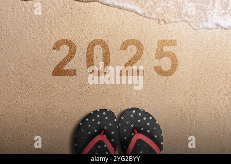 Blick von oben auf Hausschuhe und die Nummer 2025 steht auf dem Hintergrund des Strandsandes. Happy New Year Concept oder Silvester Celebration Stockfoto