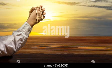 Der Mann hob die Hand, während er eine Rosenkranzperle hielt. Symbol des Glaubens und der Anbetung in Gott. Menschen christentum Gebet. Gottesdienst, Feiertag oder Konzept Stockfoto