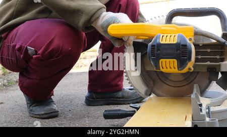 Mann in Bauhandschuhe schneiden leichte Holzplatten mit Handkreissäge, verarbeiten Holzmaterial auf Gehrungssäge Stockfoto