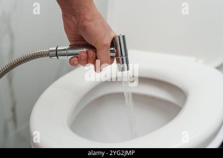Hand mit Chrom-Bidet-Dusche in einer Toilettenschüssel Stockfoto