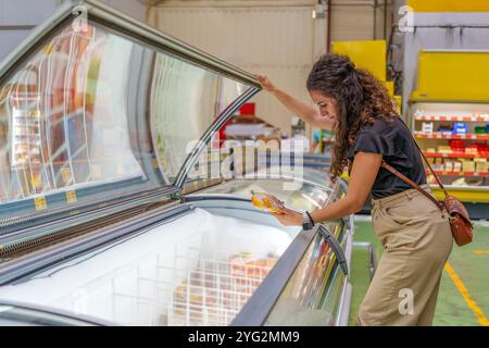 Frau mittleren Alters, die Tiefkühlprodukte in der Tiefkühlabteilung des Supermarktes auswählt Stockfoto