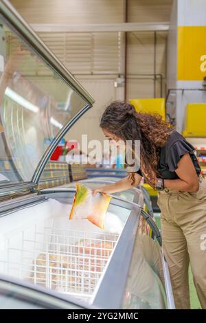 Frau mittleren Alters, die Tiefkühlprodukte in der Tiefkühlabteilung des Supermarktes auswählt Stockfoto