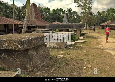 Ein Kind, das auf einer Dorfstraße spaziert, die an der Seite einer Reihe von megalithischen Gräbern im traditionellen Dorf Pasunga in Anakalang, Katikutana, Zentral Sumba, Ost-Nusa Tenggara, Indonesien gebaut wurde. Stockfoto