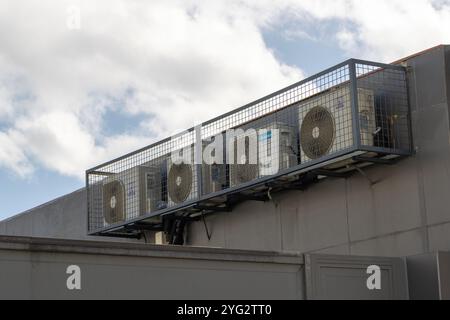 An der Außenwand eines Gebäudes sind mehrere Klimaanlagen installiert, die in einem Metallkäfig eingeschlossen sind Stockfoto