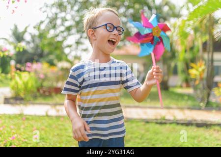 Junge in Brille spielt mit dem Windrad in einem Garten Stockfoto