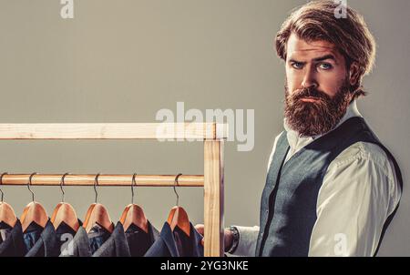 Elegant gekleideter bärtiger Mann an Händen wählt neues Kostüm im Herrenmode-Laden. Schneiderei, Schneiderei. Stylischer Herrenanzug Stockfoto