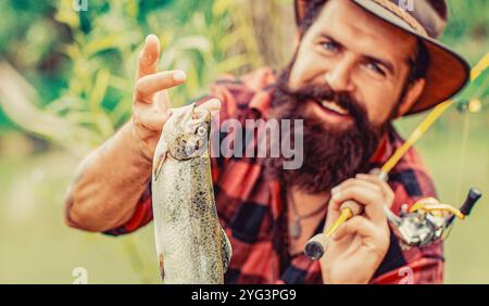 Fliegenfischer, der Forelle aus dem Wasser hält. Sportfischer zeigt seinen Fang an der Angelrute. Angler mit Angeltrophäe. Fischer Stockfoto