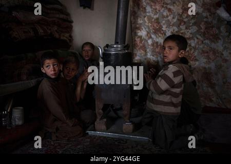 Kinder drängen sich um einen Herd, während sie versuchen, sich an einem kalten Wintermorgen in einem Binnenvertriebenen-Lager in der Hauptstadt Kabul, Afghanistan, warm zu halten Stockfoto