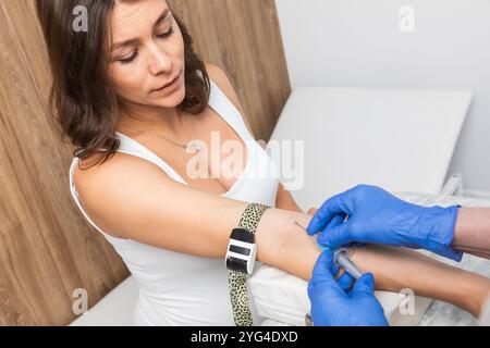 Medizinisches Fachpersonal mit Handschuhen, die bereit sind, während der Venenpunktion eine Blutprobe aus der Armvene einer schwangeren Frau mit einem Vacutainer zu entnehmen Stockfoto