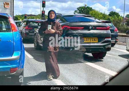 Eine Bettlerin nähert sich Autos an einer Ampel an der North Circular Road in London. Sie scheint jung und gesund zu sein, ist aber sehr aufdringlich, Geld von Fahrern zu bekommen. Einige Fahrer sind genervt und fühlen sich eingeschüchtert. Nur wenige geben ihr Geld, trotz ihrer verzweifelten Appelle. Sie nähert sich Autos, die in der wohlhabenden Gegend von Hendon sehr teuer sind. Das ist ein Kontrast zu ihrer Armut. Stockfoto