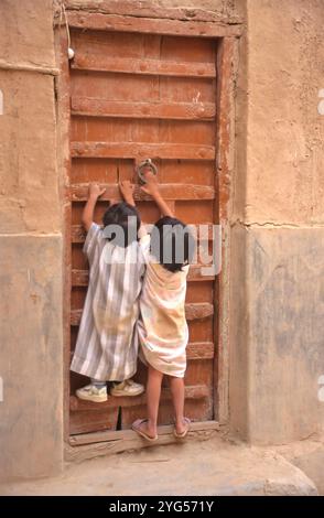 Bruder und Schwester klopfen an die Tür ihres Hauses in Shibam, Jemen Stockfoto