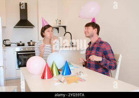 Das junge Paar feiert zu Hause gemütlich Geburtstag und genießt Kuchen und Lachen in warmer Atmosphäre. Fröhliche Atmosphäre, farbenfrohe Dekoration, Vorbereitung auf die Feiertagsparty, Dekoration Küchenraum Stockfoto