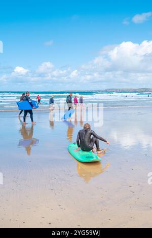 Ein müder männlicher Surfer, der eine Pause vom Surfen macht und auf seinem Surfbrett am Towan Beach in Newquay in Cornwall in Großbritannien sitzt. Stockfoto