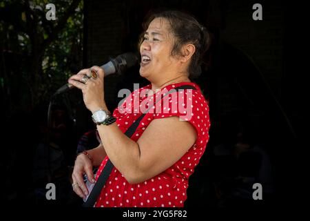 Eine asiatische Frau mittleren Alters singt Karaoke. Rotes Kleid, schwarzer Hintergrund. Singen und Tanzen sind sehr beliebte Aktivitäten in Südostasien Stockfoto