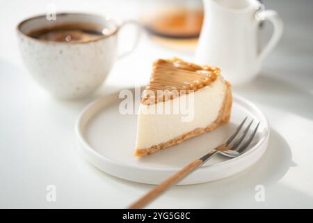 Gesalzener Karamell-Käsekuchen und eine Tasse Kaffee auf weißem Tisch. Kaffeezeit! Stockfoto