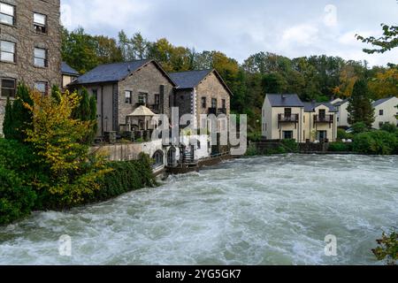 Ein Dorf neben einem Fluss in Überschwemmung, umgeben von lebhaftem Herbstlaub. Die ruhige Lage bietet Häuser am Flussufer Stockfoto