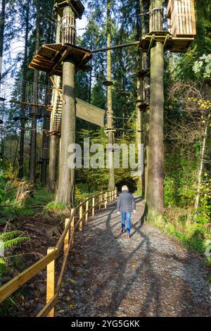 Eine hellhaarige Frau spaziert auf einem Pfad durch einen Wald mit einem Hochseilgarten. Stockfoto