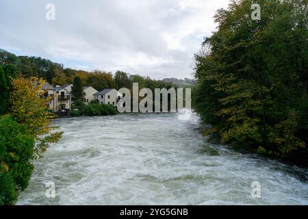 Ein Dorf neben einem Fluss in Überschwemmung, umgeben von lebhaftem Herbstlaub. Die ruhige Lage bietet Häuser am Flussufer Stockfoto