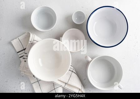 Eine schöne Anordnung minimalistischer weißer Keramikschalen auf weißer Oberfläche, ergänzt durch eine Stoffserviette. Draufsicht. Schüsseln Kollektion Stockfoto