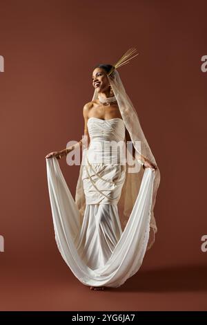 Eine atemberaubende afroamerikanische Frau strahlt Anmut aus in einem fließenden weißen Kleid, das mit Perlen verziert ist und ihre Eleganz zum Ausdruck bringt. Stockfoto