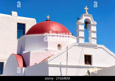 Mykonos, Griechenland - 7. Mai 2024: Orthodoxe Kirche mit roter Kuppel und Glockenturm auf Mykonos, Griechenland, vor klarem blauem Himmel *** Orthodoxe Kirche mit roter Kuppel und Glockenturm auf Mykonos, Griechenland, vor klarem, blauem Himmel Stockfoto