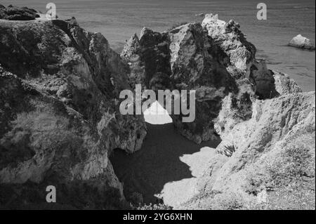 Schwarz-weiß-Blick auf den natürlichen Felsbogen in praia da rocha, der einen abgelegenen Strand und das Meer in starkem Kontrast umrahmt Stockfoto