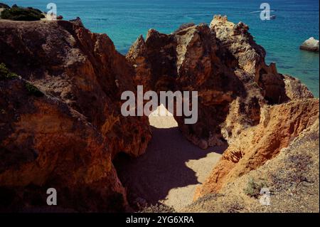 Der Felsenbogen führt zu einem Strand, der von Sonnenlicht getaucht und von lebhaften Blautönen des Ozeans umgeben ist Stockfoto